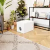A white cat litter box is placed on a wooden floor next to a rug and several potted plants, with a shelf unit in the background. Náhled obrázku produktu