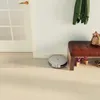 A robot vacuum cleaner is cleaning the floor in a hallway next to a bench with shoes and a bag on it. Voir les images du produit