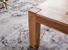 A close-up of a wooden table leg and corner on a patterned rug. Produktbild-Vorschau