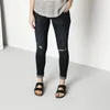 A person wearing dark wash ripped jeans and black Birkenstock sandals. Produktbild-Vorschau