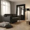 A dark gray fabric sofa is shown in a well-lit living room with a large ornate black mirror and a floor lamp. Voir les images du produit