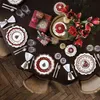 A beautifully set dining table with Christmas-themed plates, cutlery, napkins, gifts, and flowers. Produktbild-Vorschau
