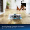 A robot vacuum cleaner is mopping a wooden floor in a home, with a dog in the background. Produktbild-Vorschau