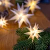 A close-up shot of a string of star-shaped LED lights intertwined with evergreen branches, set against a wooden surface. Produktbild-Vorschau