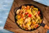 A close-up view of a pan filled with mixed vegetables, placed on a wooden surface with a blue background. Produktbild-Vorschau