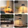 Collage of four images showing a black cordless LED table lamp in different settings: on a bedside table, on a shelf with a plant, on outdoor tables, and on a dining table. Náhľad obrázku produktu