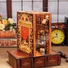 A miniature diorama of a bookstore, designed to fit between books on a shelf, is displayed on top of a larger, decorative book. Voir les images du produit