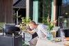 A man is using a gas pizza oven on a patio. Produktbild-Vorschau