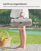 A person holding a folded picnic blanket outdoors with a basket of flowers nearby. Produktbild-Vorschau