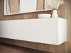 A white floating TV cabinet mounted on a wooden wall, with a decorative bowl and vase with flowers on top. Produktbild-Vorschau