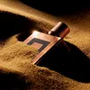 A copper-colored perfume bottle is partially buried in sand, with dramatic lighting. Anteprima dell’immagine prodotto