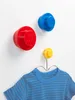 Three LEGO-style wall hooks are mounted on a white wall. A blue and black striped t-shirt is hanging on the smallest yellow hook. Produktbild-Vorschau