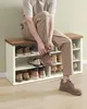A man is sitting on a shoe bench and tying his shoes. The shoe bench has multiple shelves filled with shoes. Náhled obrázku produktu