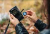 A person is holding a camera and inserting an SD card into it. Produktbild-Vorschau