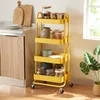 A yellow kitchen trolley filled with jars and plates, placed next to a kitchen counter with cutting boards. Produktbild-Vorschau