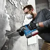A man is using a blue and black rotary hammer drill to break apart a concrete wall. Produktbild-Vorschau