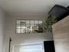 A mirror with a grid design is mounted on a wall above a sheer curtain. A plant and part of a desk are visible to the right. Produktbild-Vorschau