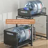 A two-tier black metal organizer rack holding large water bottles, placed on a wooden surface with a marble-tiled wall in the background. Produktbild-Vorschau