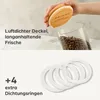 A hand holding a lid over a glass jar filled with coffee beans, with text describing the product's features and a separate image of extra sealing rings. Produktbild-Vorschau