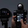 A hand is holding a Sekonic light meter, with a Godox light in the background. Náhľad obrázku produktu