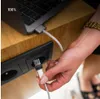 A person is plugging a white USB-C cable into a black power outlet on a wooden desk, with a laptop in the background. Produktbild-Vorschau