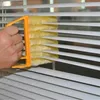 Orange-gelber Jalousie-Abstauber, von einer Hand gehalten, reinigt weiße Jalousien Anteprima dell’immagine prodotto