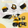 A yellow toy excavator with black accents, shown outdoors with a blurred background of a house and garden. Náhled obrázku produktu