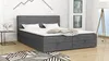 A grey boxspring bed with white bedding and pillows is shown in a room with a white brick wall and wooden floor. Produktbild-Vorschau