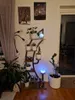 A plant stand with multiple plants and decorative items is shown in a room with wooden floors and a curtain. Náhľad obrázku produktu