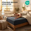 A woman sleeping peacefully on a bed with a dark blue fitted sheet. Produktbild-Vorschau