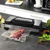 A vacuum sealer is shown on a kitchen counter with a piece of meat in a vacuum bag, along with some vegetables and spices. Anteprima dell’immagine prodotto