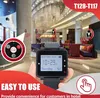 A hand holding a smartwatch-like receiver in a hotel lobby, with several wireless call buttons mounted on pillars in the background. Náhled obrázku produktu