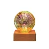 A decorative LED lamp with a glass sphere displaying a firework-like pattern, resting on a wooden base. Produktbild-Vorschau