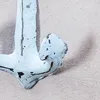 A close-up of a light blue anchor with black distressed markings, resting on a sandy surface. Produktbild-Vorschau