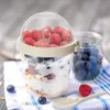 A yogurt cup filled with yogurt, granola, blueberries, and raspberries, placed on a striped cloth next to a glass jar of blueberries and a spoon. Voir les images du produit