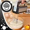 A hand mixer is shown in use, mixing batter in a glass bowl, with eggs and pastries visible in the background. Produktbild-Vorschau