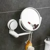 A white suction cup makeup mirror mounted on a gray tiled wall, with a makeup brush hanging from it. Produktbild-Vorschau