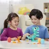 Two children are playing with Play-Doh dinosaur toys on a table. Produktbild-Vorschau