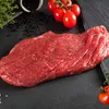 A raw flank steak is presented on a dark slate surface, with tomatoes, peppercorns, and herbs as garnishes. Produktbild-Vorschau