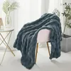 A dark gray plush blanket draped over a pink chair, with a small table and plant in the background. Produktbild-Vorschau