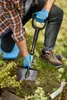 A person is kneeling in a garden, using a shovel to dig into the soil. Produktbild-Vorschau