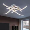 A modern ceiling light fixture with multiple curved arms emitting a soft white light, mounted on a ceiling in a room with brown walls and a window. Produktbild-Vorschau