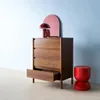 A wooden chest of drawers with an open drawer, a red lamp, and a red stool against a light blue wall. Anteprima dell’immagine prodotto