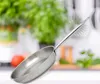 A stainless steel frying pan is shown in focus against a blurred background of a kitchen with greenery and food items. Anteprima dell’immagine prodotto