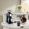 A coffee setup with a grinder, pour-over brewer, and storage canisters on a table. Náhled obrázku produktu