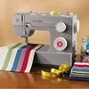 A sewing machine is shown on a wooden table with fabric and a measuring tape. Anteprima dell’immagine prodotto
