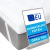 A white mattress topper on a gray bed base, with a blue and white marketing label in the foreground. Náhled obrázku produktu