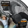 A woman is relaxing on a couch with a laptop while a large fan is operating in the background. Anteprima dell’immagine prodotto