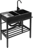 A black freestanding kitchen sink with a faucet and a draining board, shown from a three-quarter angle against a white background. Produktbild-Vorschau