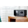 A black digital radio is placed on a wooden table in front of white blinds. Produktbild-Vorschau